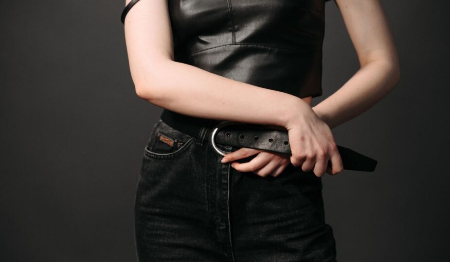 Närbild av svart läderbälte med runt spänne till svarta jeans